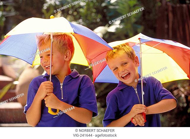 portrait, half-figure, two blond 5-year-old twin-boys wearing blue t-shirts with multi-coulered umbrellas in their hands  - GERMANY, 30/05/2004