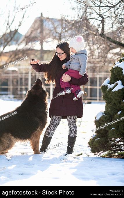 Mom and little daughter walking in a winter day and play with her dog