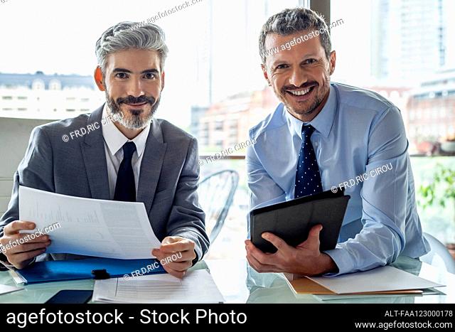 Smiling businessmen holding document and digital tablet
