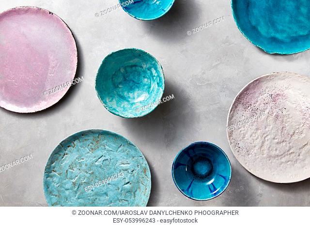 Ceramic bowls of different colors, sizes and types are empty on a gray concrete background. Flat lay of porcelain dishes handmade