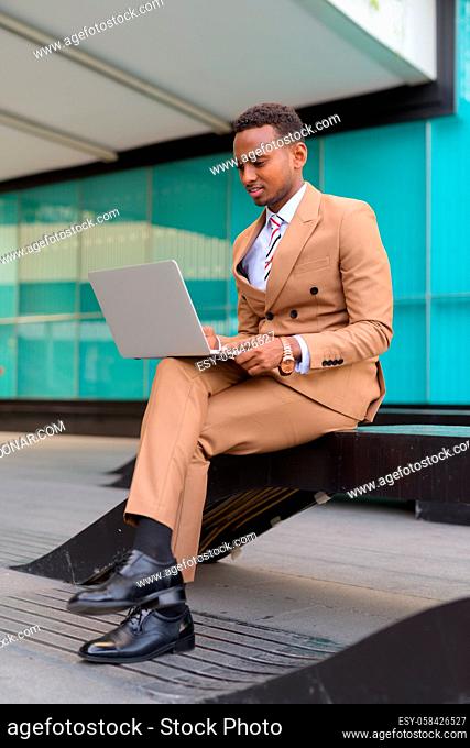 Portrait of young handsome African businessman wearing suit outside modern building in the city