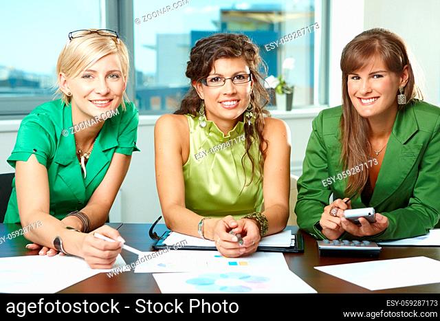 Group of attractive businesswomen sitting at meeting room, discussing financial charts on table, smiling