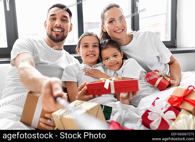 family with christmas gifts taking selfie in bed