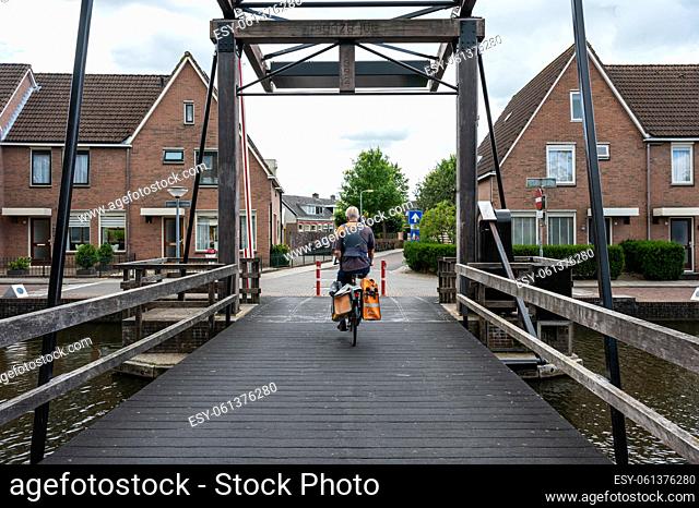 Meppel, Overijssel, The Netherlands - Post office delivery man driving his bike over an old bridge