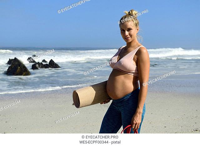 Portrait of active pregnant woman holding gym mat on the beach