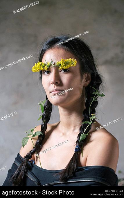 Confident young woman with flower stuck on forehead and plants in braided hair