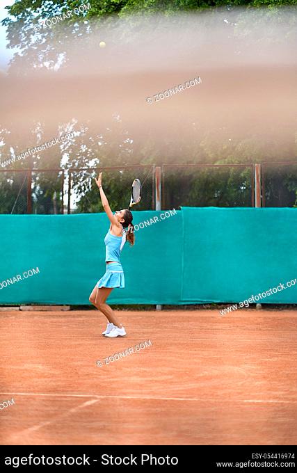 Gorgeous girl plays tennis on the court outdoors. She prepares to beat off a ball. Woman wears a light blue sportswear with white sneakers. Vertical