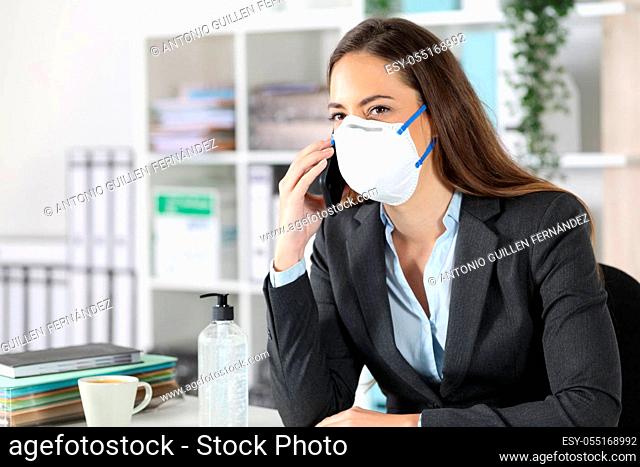 Executive woman calling on smart phone avoiding coronavirus with mask sitting on a desk at office