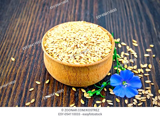 Linen seeds white in a bowl and blue flax flower on a wooden plank background