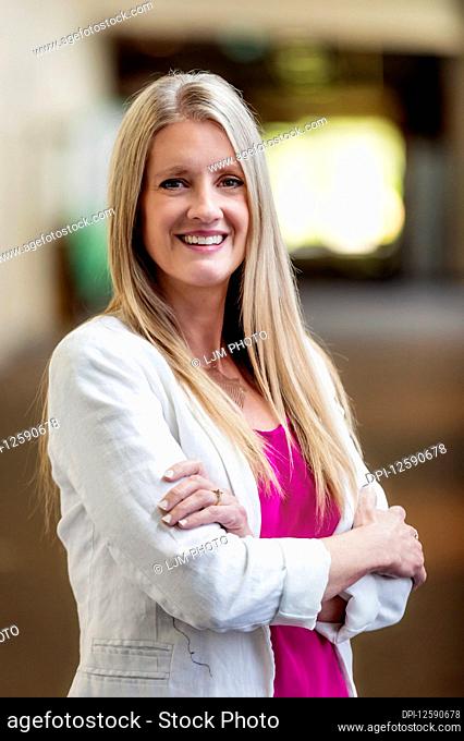 A professional mature business woman with her arms crossed, posing for the camera in a hallway; Edmonton, Alberta, Canada