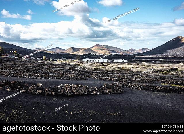 Traditional white houses in black volcanic landscape of La Geria wine growing region with view of Timanfaya National Park in Lanzarote