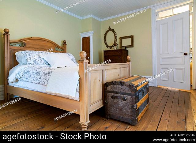 Queen size bed with wooden headboard and footboard, antique travel chest, dresser in upstairs master bedroom with oil stained fir wood floorboards inside an old...