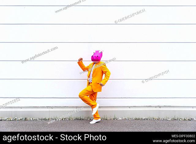 Man wearing vibrant orange suit and hippo mask jogging in front of white wall