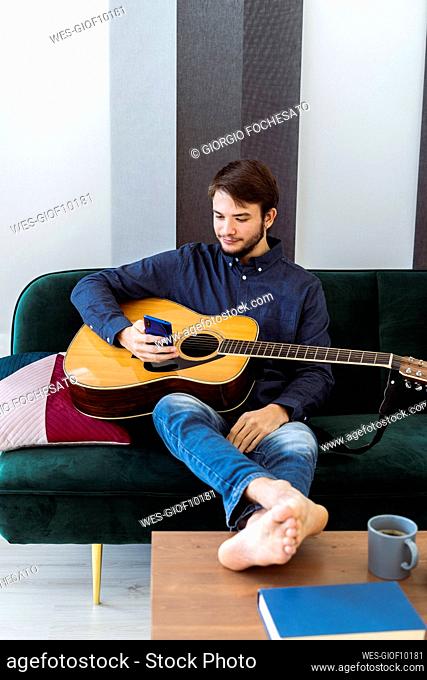Guitarist using mobile phone while sitting with guitar on sofa at studio
