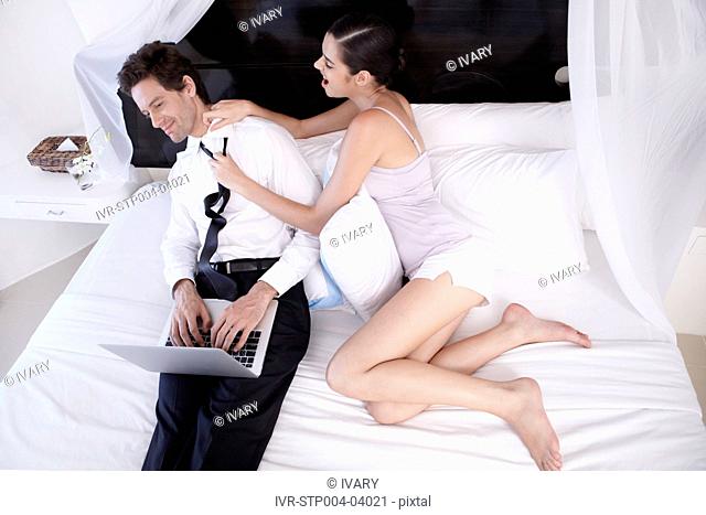 A young couple sitting on a bed with a laptop