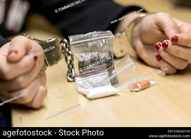 Photo of a Caucasian woman, handcuffed to her wrists for being found in possession of various illegal drugs, placed in front of her
