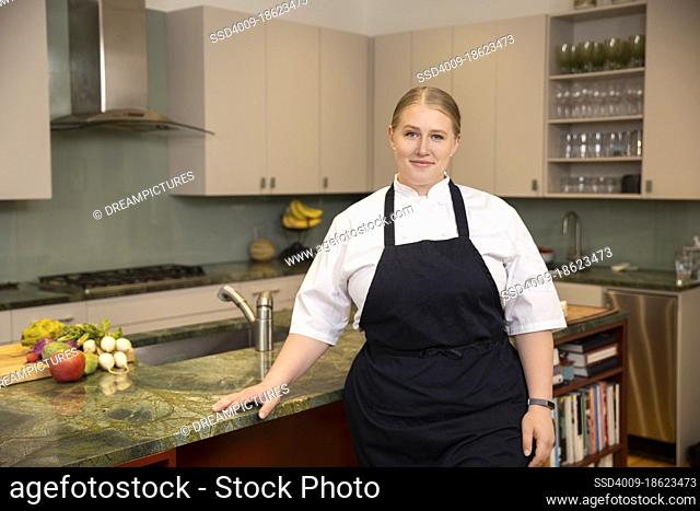 Confident portrait of Chef Megan Gill in home kitchen looking at camera, with cook books on shelf behind her
