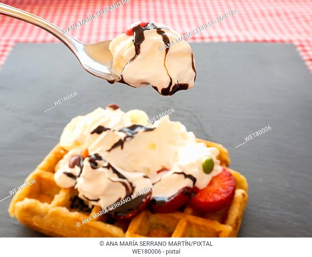 Taking a tablespoon of cream in a waffle with strawberries, whipped cream, chocolate syrup and candy colors