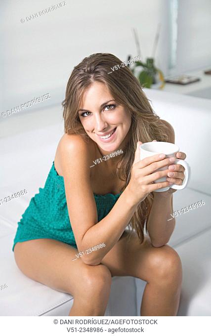 Portrait of a blonde woman at home with a cup of coffee smiling at camera in the living room