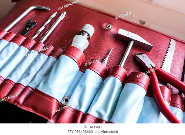 a small hammer, a screwdriver, nippers, saw and fixing pen in red in old vintage leather case right side view. Man's tricks concept