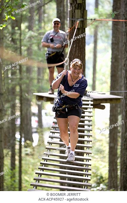 A smiling woman makes her way across one of the rope bridges at the Wildplay Elements adventure park near Nanaimo. Central Vancouver Island, British Columbia