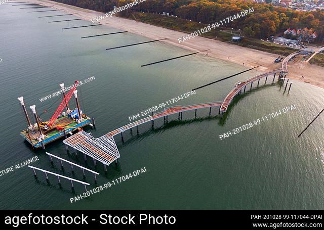 28 October 2020, Mecklenburg-Western Pomerania, Koserow: With a mobile crane on a pontoon, the new sea bridge is being built on the beach of the island of...