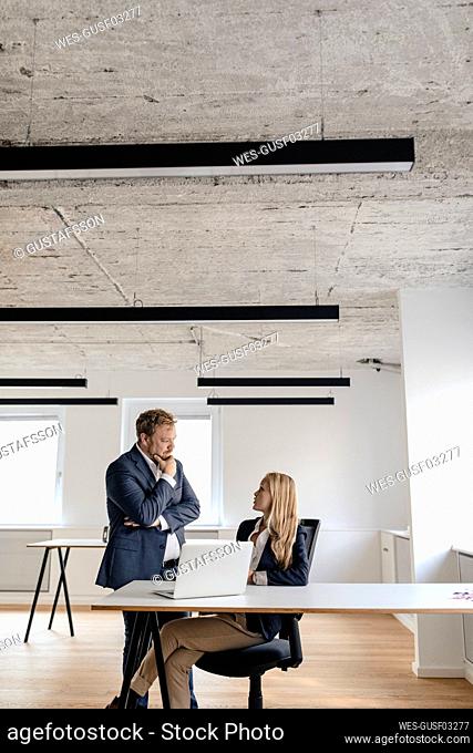 Businessman and businesswoman talking at desk in office
