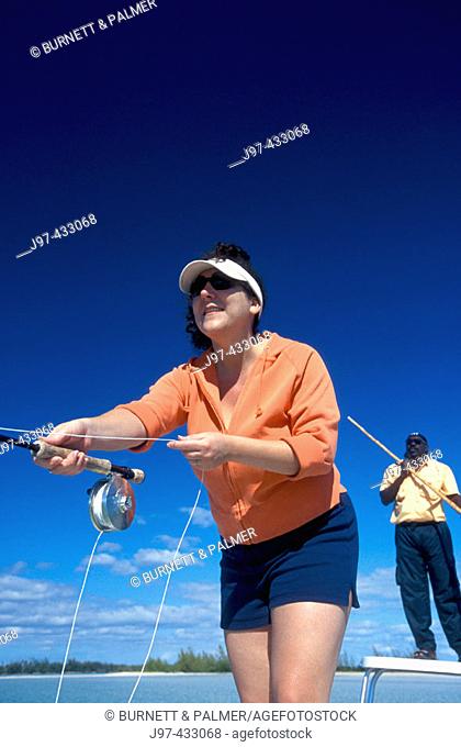 A woman enjoying the sport of fly fishing with her guide poling throught the flats of Blanket Sound off Kamalama Cay, Andros, Bahamas, Atlantic Ocean