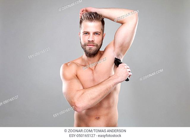 Handsome young bearded man with a trimmer shaving off body hair