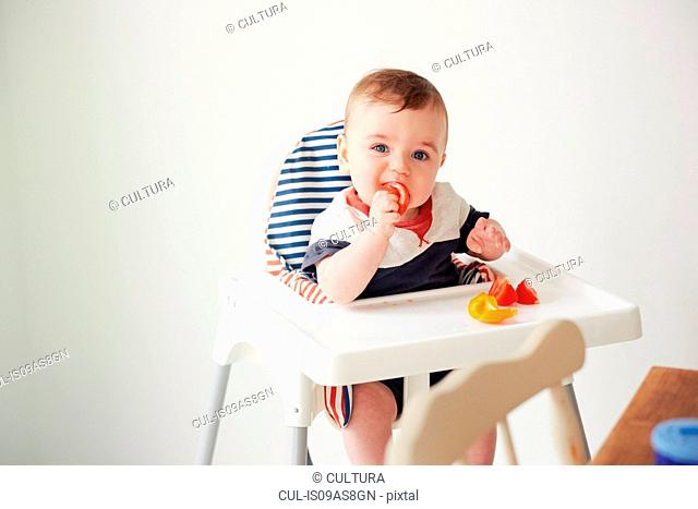 Baby boy feeding himself in baby chair