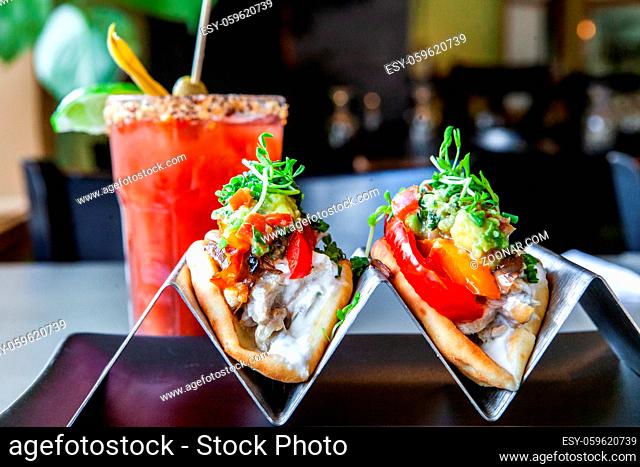 A closeup and front view of two healthy tacos filled with fresh vegetables, served with a refreshing and fruity cocktail inside a trendy restaurant