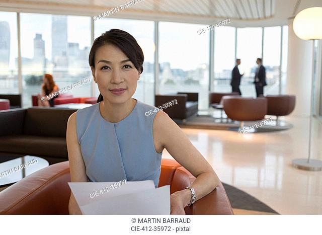 Portrait confident businesswoman reviewing paperwork in office lounge