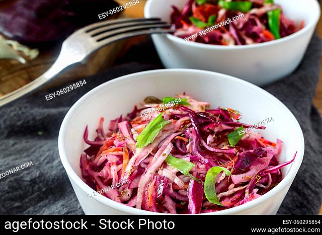 On a wooden table on a napkin, a salad of red and white cabbage with green onions. The concept of healthy eating. Close up