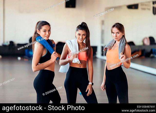 Three happy smiling positive girls after training in the gym. There are looking at camera. Horizontal