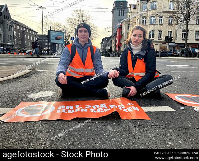 17 March 2023, Cologne: An activist and an activist sit on a street in Cologne. Activists from the climate group Last Generation got stuck on a major traffic...