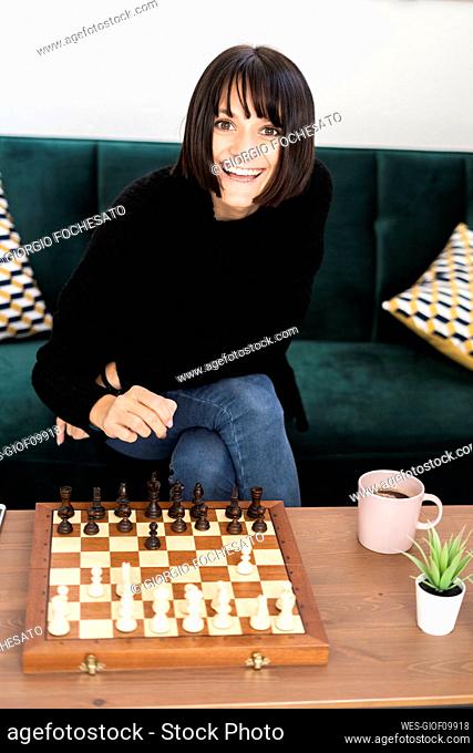 Happy woman with coffee cup playing chess in living room