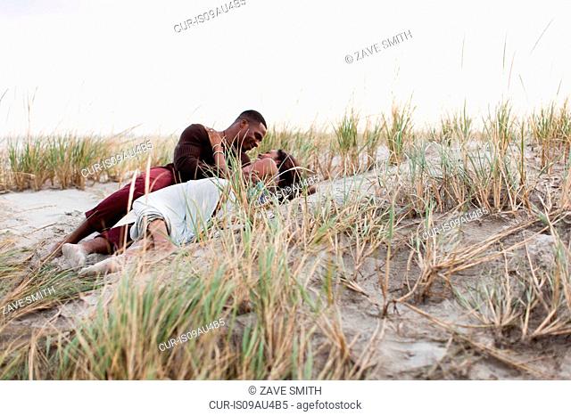Couple lying in sand dunes, face to face