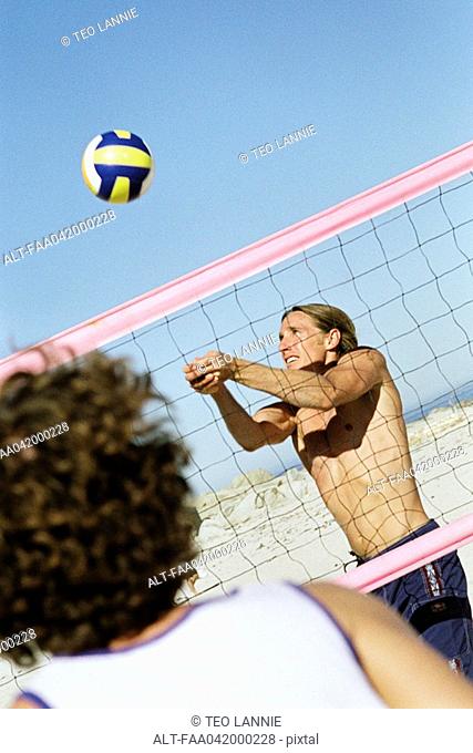 Male playing beach volleball, preparing to hit ball
