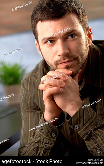 Serious young man looking determined sitting with hands folded
