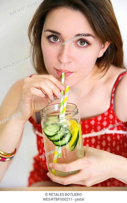 Portrait of woman drinking detox water infused with lemon and cucumber