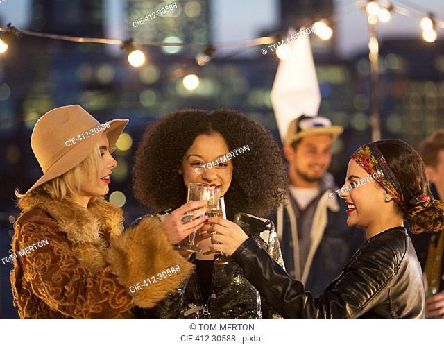 Young women toasting champagne glasses at nighttime rooftop party