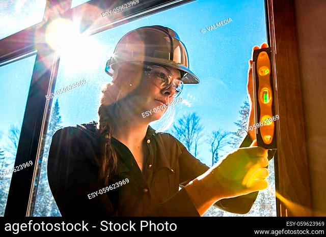 close up on worker woman uses spirit level on vertical surface next to a window with sun in the sky view. construction inspector, architect concepts