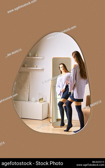 Reflection in mirror of young woman standing in front of the mirror