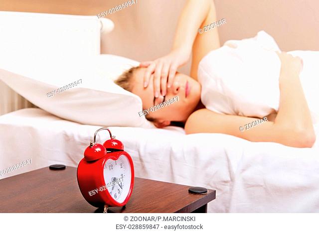 Young woman trying to sleep when alarm clock ringing