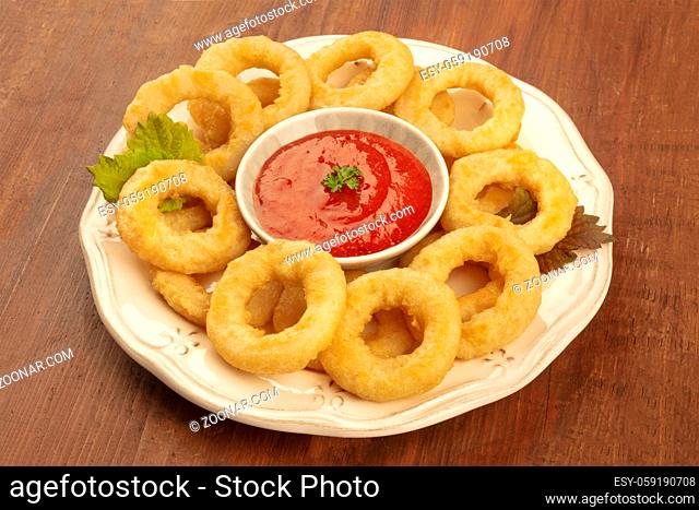 A closeup photo of squid rings with a tomato sauce on a dark wooden background