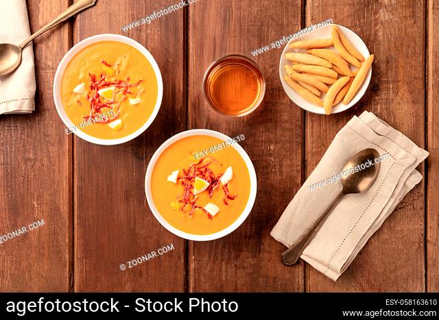 Salmorejo, Spanish cold tomato soup, shot from the top on a dark rustic wooden background with picos, typical breadsticks, and wine