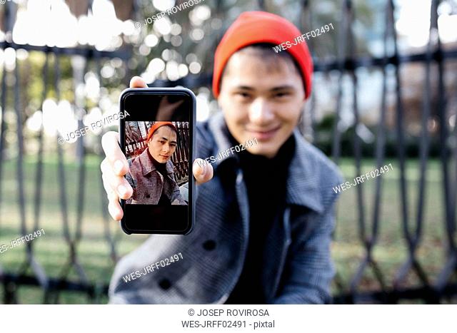 Young man showing mobile phone with portrait of himself