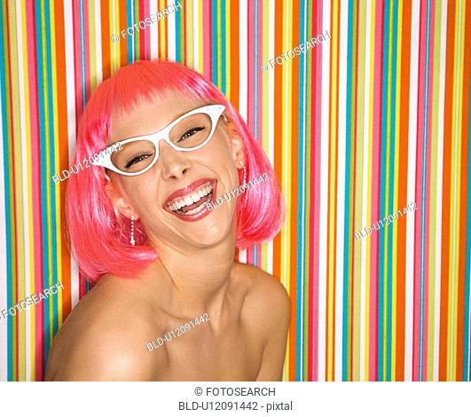Portrait of attractive Caucasian young adult woman wearing pink wig against striped background making sassy expression looking at viewer