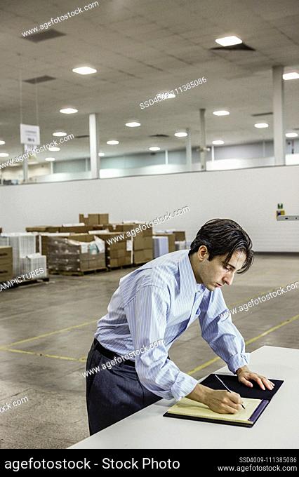 Businessman writing on pad in warehouse