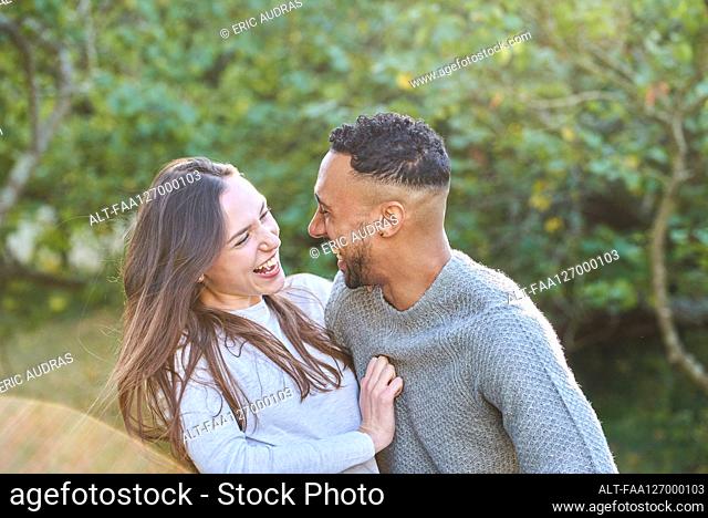 Smiling young couple looking at each other in public park